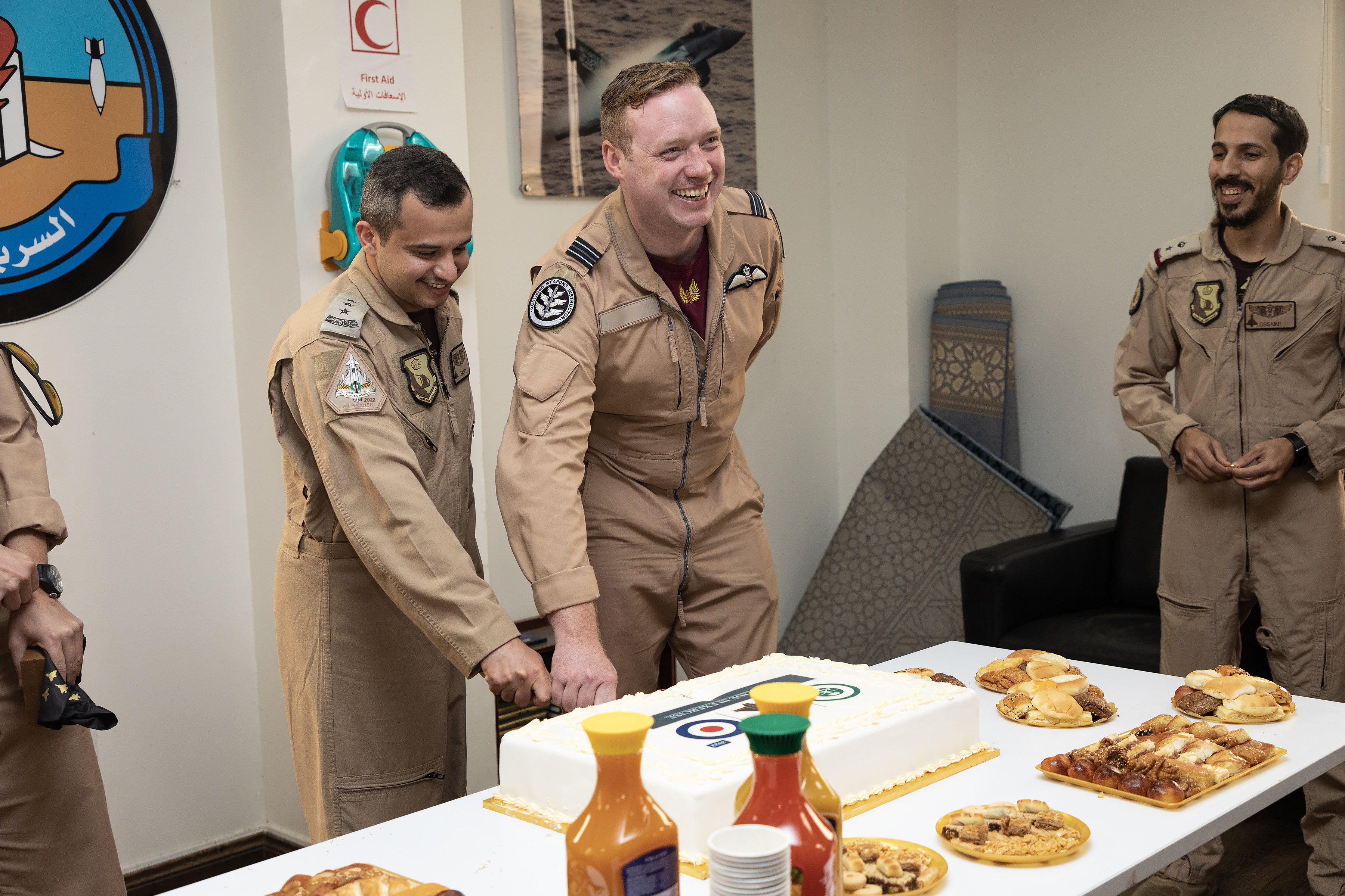 Image shows personnel cutting a cake on a table with Arabian dishes and sauces.